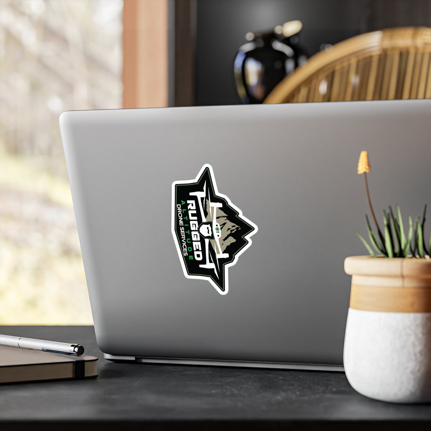 Laptop with rugged drone service vinyl decals sticker on the back near a plant and notebook